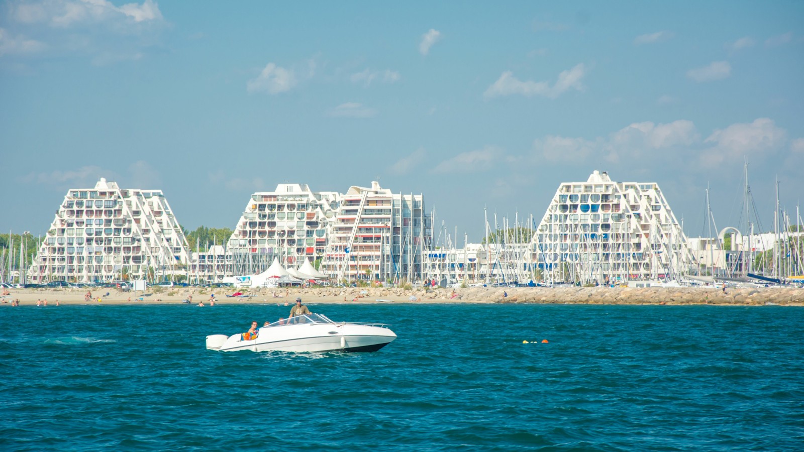 White triangular shaped buildings sitting on a sandy beach with blue skies
